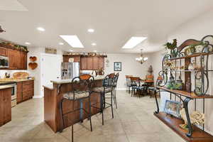 Kitchen featuring a skylight, light stone counters, a notable chandelier, a kitchen bar, and appliances with stainless steel finishes