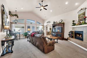 Living room featuring ceiling fan with notable chandelier, french doors, light carpet, and a tiled fireplace