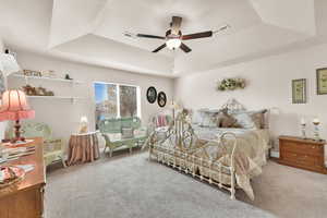 Bedroom featuring light colored carpet, a raised ceiling, and ceiling fan