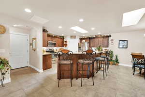 Kitchen featuring a kitchen bar, appliances with stainless steel finishes, a skylight, and a center island with sink