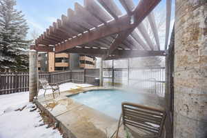 Snow covered pool with a pergola and a hot tub