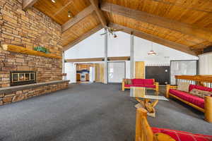 Carpeted living room featuring beam ceiling, ceiling fan, a stone fireplace, high vaulted ceiling, and wood ceiling