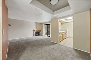 Unfurnished living room featuring sink, light colored carpet, a fireplace, and a tray ceiling