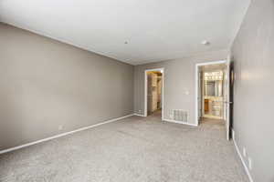 Unfurnished bedroom with a walk in closet, a closet, ensuite bath, and light colored carpet