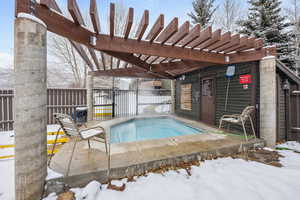 Snow covered pool featuring a jacuzzi and a pergola