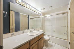 Full bathroom with tile patterned floors, vanity, bath / shower combo with glass door, and toilet