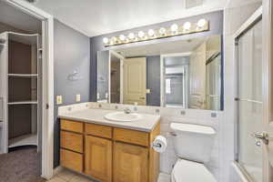 Full bathroom featuring vanity, shower / bath combination with glass door, tile patterned floors, toilet, and tile walls