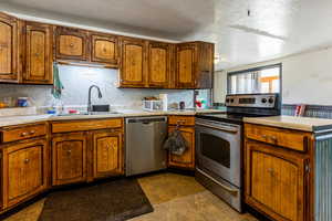 Kitchen featuring sink, a textured ceiling, appliances with stainless steel finishes, tasteful backsplash, and kitchen peninsula