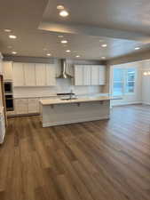 Kitchen with white cabinetry, dark wood-type flooring, wall chimney range hood, and appliances with stainless steel finishes