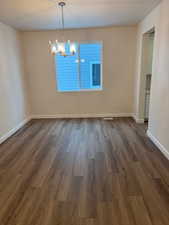 Unfurnished dining area with dark hardwood / wood-style floors and an inviting chandelier