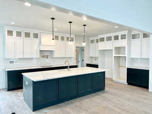 Kitchen featuring a large island, light stone counters, light hardwood / wood-style floors, decorative light fixtures, and white cabinets