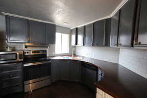 Kitchen featuring tasteful backsplash, ornamental molding, stainless steel appliances, dark wood-type flooring, and sink