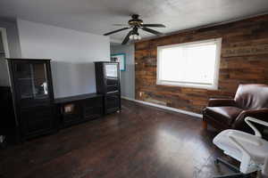 Sitting room with ceiling fan, dark wood-type flooring, and wooden walls