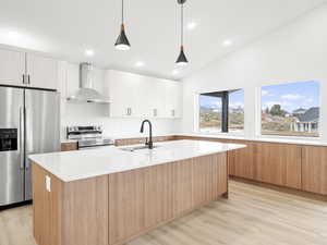 Kitchen with white cabinets, wall chimney exhaust hood, sink, and appliances with stainless steel finishes