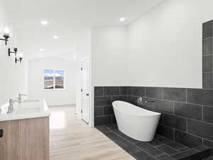 Bathroom with hardwood / wood-style floors, a tub, tile walls, and lofted ceiling