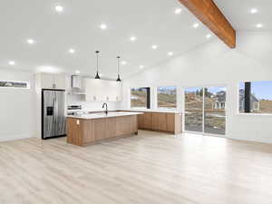 Kitchen featuring light wood-type flooring, wall chimney exhaust hood, stainless steel appliances, a kitchen island with sink, and white cabinets