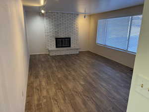 Unfurnished living room featuring a fireplace, rail lighting, ceiling fan, and dark wood-type flooring