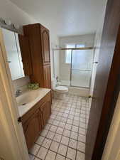 Full bathroom with toilet, tile patterned flooring, vanity, and combined bath / shower with glass door