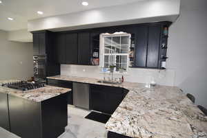 Kitchen featuring sink, decorative backsplash, light stone countertops, kitchen peninsula, and stainless steel appliances