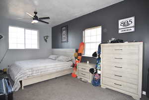 Bedroom with ceiling fan, a textured ceiling, and dark colored carpet