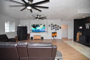 Living room with a textured ceiling, hardwood / wood-style flooring, a wood stove, and ceiling fan