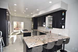 Kitchen with kitchen peninsula, backsplash, light stone counters, and sink