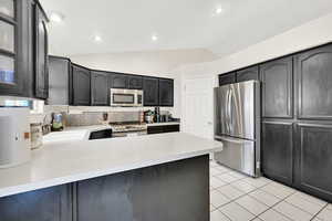 Kitchen featuring sink, vaulted ceiling, decorative backsplash, light tile patterned floors, and appliances with stainless steel finishes