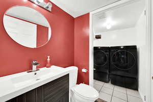 Bathroom featuring vanity, tile patterned flooring, toilet, independent washer and dryer, and a textured ceiling