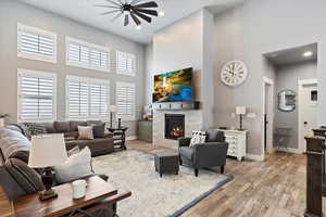 Living room featuring a fireplace, a high ceiling, light hardwood / wood-style floors, and ceiling fan