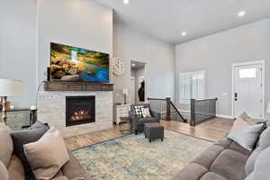 Living room with wood-type flooring, a towering ceiling, and a stone fireplace