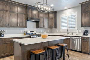 Kitchen featuring light wood-type flooring, appliances with stainless steel finishes, a textured ceiling, and a center island