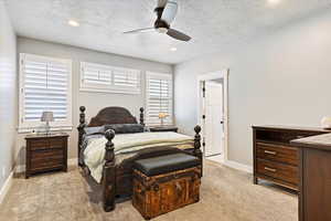 Bedroom featuring ceiling fan, light colored carpet, a textured ceiling, and multiple windows