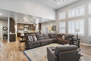 Living room with ceiling fan with notable chandelier, a towering ceiling, light hardwood / wood-style floors, and a textured ceiling