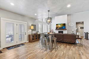 Dining area with an inviting chandelier, a stone fireplace, a textured ceiling, and light hardwood / wood-style flooring