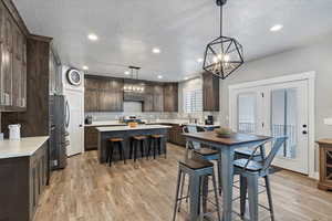 Kitchen featuring appliances with stainless steel finishes, dark brown cabinetry, decorative light fixtures, light hardwood / wood-style flooring, and a kitchen island