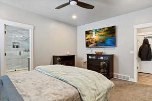 Carpeted bedroom featuring a textured ceiling, a closet, ceiling fan, and connected bathroom