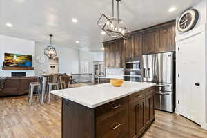 Kitchen with decorative light fixtures, a kitchen island, appliances with stainless steel finishes, and light hardwood / wood-style flooring