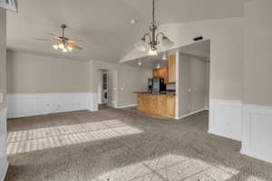 Unfurnished living room with vaulted ceiling, dark carpet, ceiling fan with notable chandelier, and washer / dryer