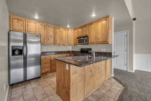 Kitchen with dark stone counters, sink, light colored carpet, kitchen peninsula, and stainless steel appliances