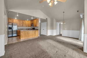 Kitchen featuring appliances with stainless steel finishes, ceiling fan with notable chandelier, light colored carpet, and hanging light fixtures