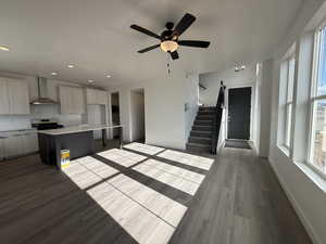 Kitchen with a breakfast bar, a center island, dark wood-type flooring, stainless steel range with gas cooktop, and wall chimney exhaust hood