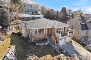 View of front facade with driveway, a garage, a shingled roof, stone siding, and a front yard