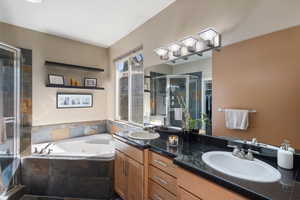 Full bathroom featuring a whirlpool tub, double vanity, a stall shower, and a sink