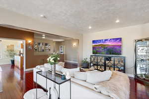 Living room featuring a textured ceiling, baseboards, dark wood-type flooring, and recessed lighting