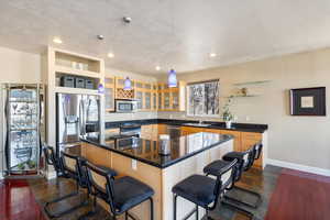 Kitchen featuring dark countertops, appliances with stainless steel finishes, glass insert cabinets, a sink, and a kitchen breakfast bar