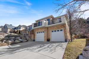 View of front of property with concrete driveway, a balcony, stone siding, an attached garage, and stucco siding