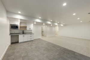 Great room with kitchenette white cabinets, light carpet, stainless steel microwave, and sink