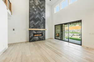 Great room featuring a healthy amount of sunlight, a towering ceiling, a fireplace, and light hardwood / wood-style flooring