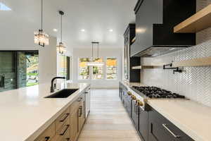 Kitchen with decorative backsplash, custom exhaust hood, sink, white oak cabinets, and hanging light fixtures