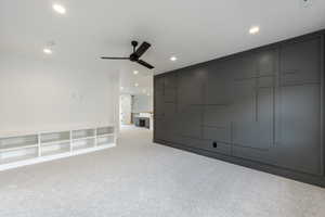 Carpeted great room featuring ceiling fan and geo geo style wall